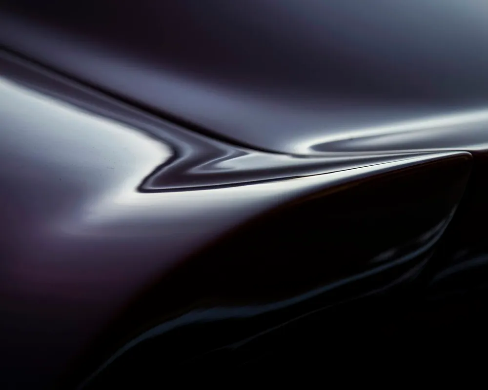 Aile de carrosserie sombre dans la pénombre, parcourue par un filet de lumière rasante qui suit le pli de tôle et s'y déforme