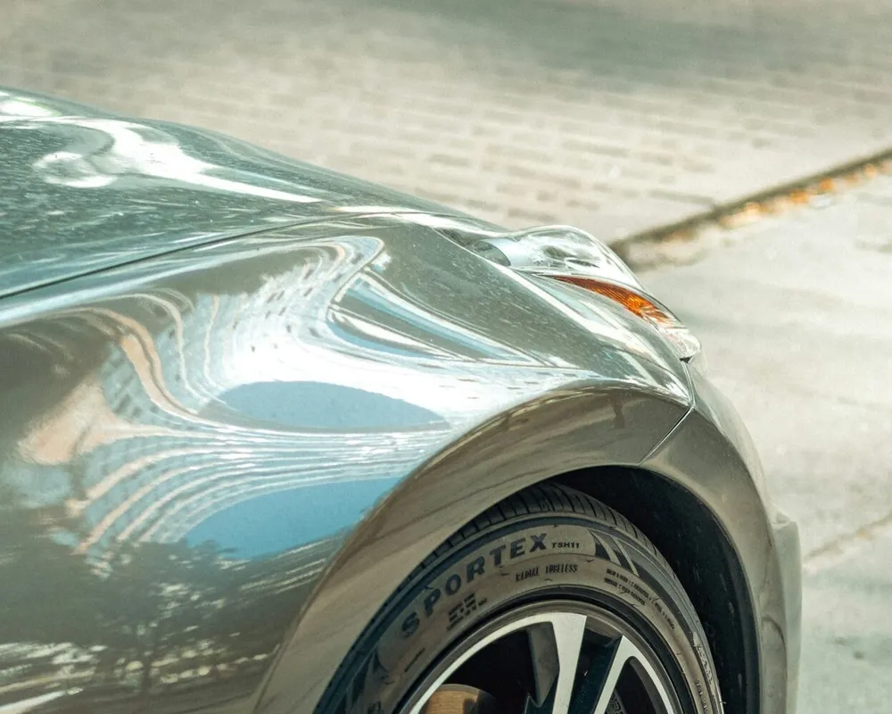 Aile avant d'une automobile grise, les reflets se courbant le long de la ligne de style